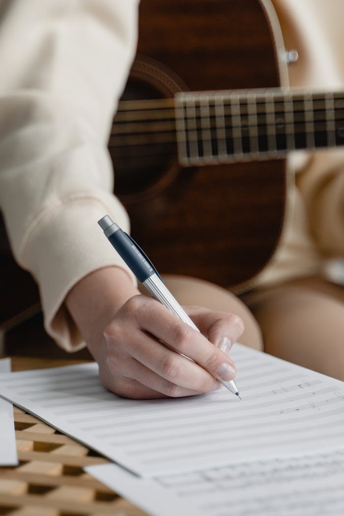 About Close-up of a woman writing music notes with guitar in background.